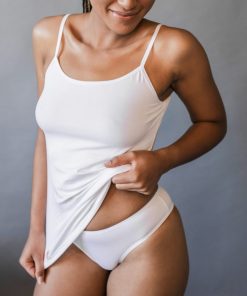 Modelka nadvihuje biele bambusové tielko s úzkymi ramienkami nad bielymi nohavičkami.