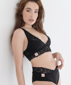 Modelka opretá o bielu stenu v čiernej čipkovej bralette Diana a nohavičkách Ala s čipkou v páse.